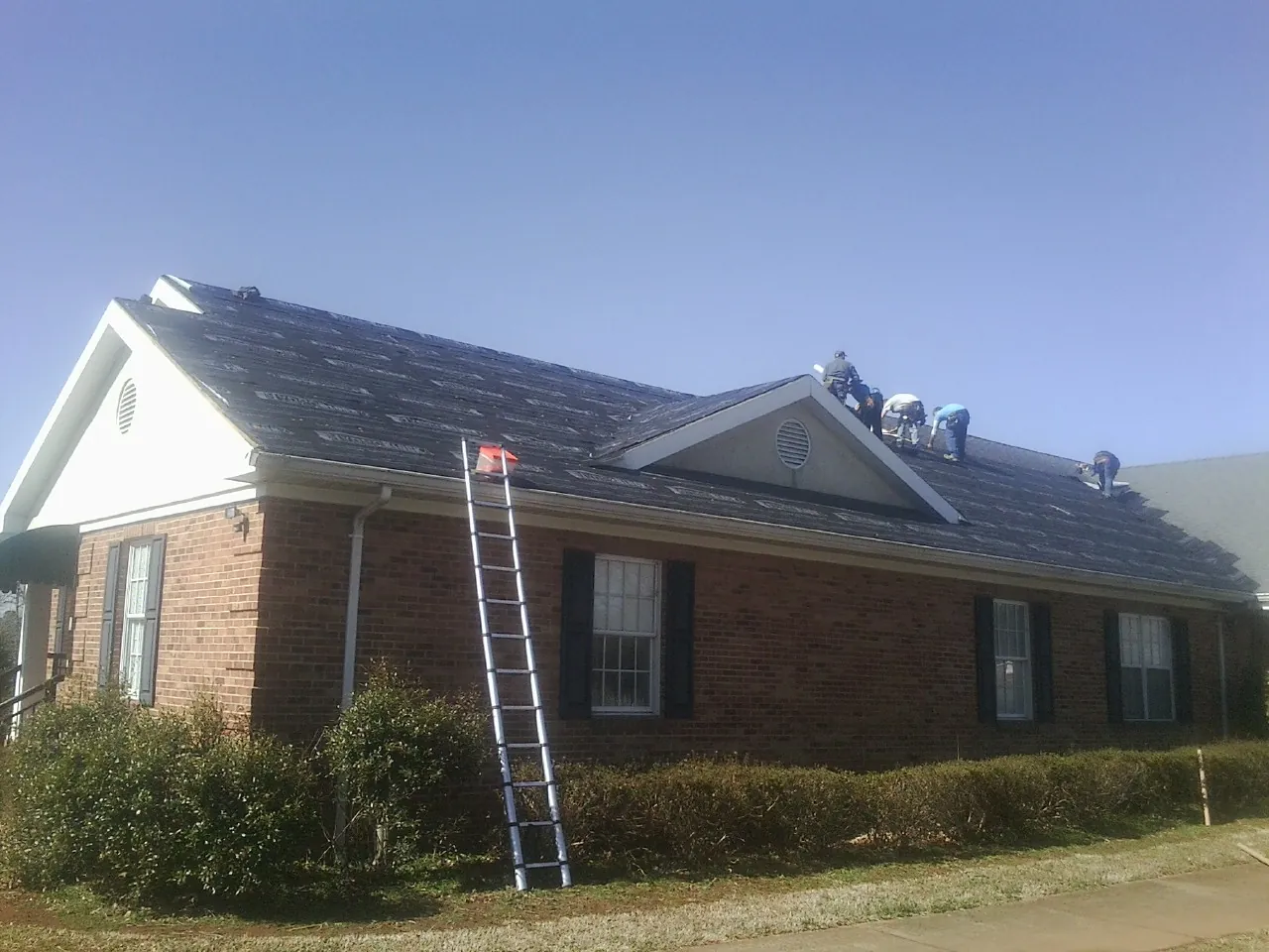 Crew tearing shingles off a brick ranch roof with a ladder set — Metal Roof Repair work by our crew in Christiana
