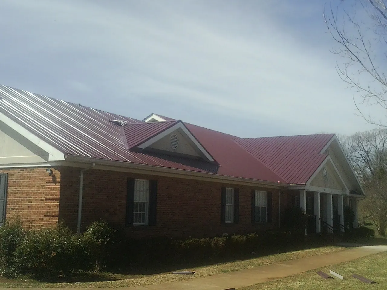 Red metal roof with gabled entries on a long brick building, from a Hail Damage Roof Repair job in Christiana