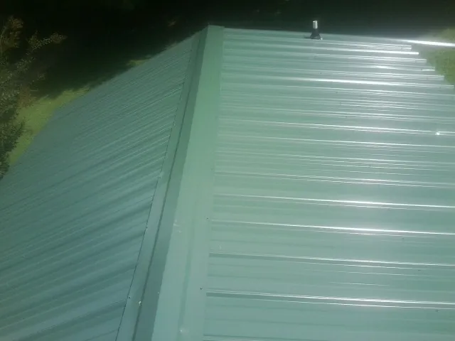 New green metal panels meeting at the ridge of a roof — Flat Roof Repair work by our crew in Christiana